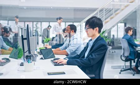 Shot of a Young Japanese Business Specialist Works on Desktop Computers. Diverse Team of Young and Motivated Businesspeople in Modern Open Office. Stock Photo