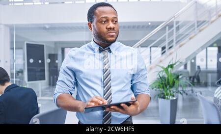 Handsome Young Black Manager in a Shirt Walking Pass His Business Colleagues with a Tablet. Diverse and Motivated Business People Work on Computers in Stock Photo
