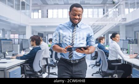Handsome Young Black Manager in a Shirt Walking Pass His Business Colleagues with a Tablet and Supervise Their Work. Diverse and Motivated Business Stock Photo
