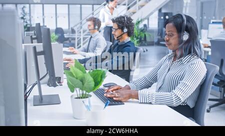 Team of Handsome and Beautiful Diverse Multicultural Customer Service Operators Working at a Busy Modern Call Center with Specialists Wearing Headsets Stock Photo
