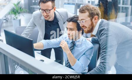 In Bright Modern Office: Businessman Sitting and Working at His Desktop Computer, Project Manager and Team Leader Standing Beside Him. They Have Stock Photo
