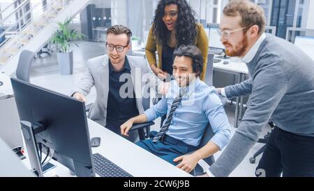 Handsome Businessman Uses Desktop Computer, Cheerfully Celebrates Successful Business Transaction and New Client Contract Signing. His Team Members Stock Photo