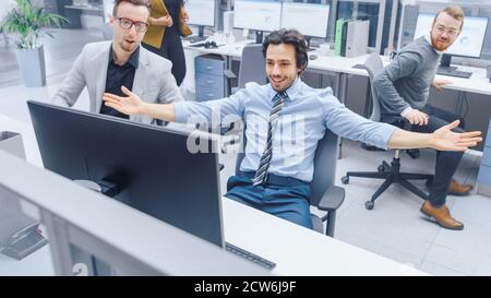 Handsome Businessman Uses Desktop Computer, Cheerfully Celebrates Successful Business Transaction and New Client Contract Signing. His Team Members Stock Photo