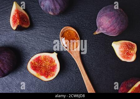 Fig jam in a wooden spoon and fresh figs on black stone background, top view Stock Photo