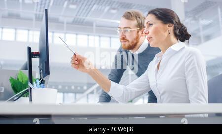 Beautiful Businesswoman Uses Desktop Computer, Consults Her Project Manager about Documents with Graphs and Statistics. In the Background Big Stock Photo