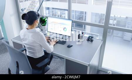 In Open Space Office Businesswoman Working on Her Personal computer with Financial Data, Graphs and Statistics. Shot in Big Bright Modern Open Space Stock Photo