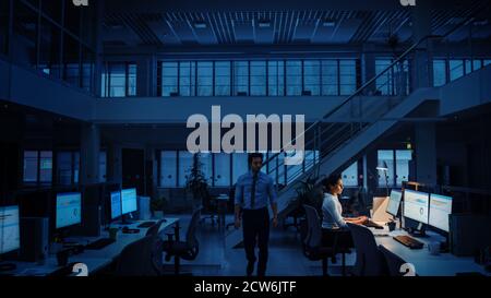 Working Late at Night in the Office: Businesswoman Using Desktop Computer, Analyzing, Using Documents, Solving Problems, Finishing Project. Colleague Stock Photo