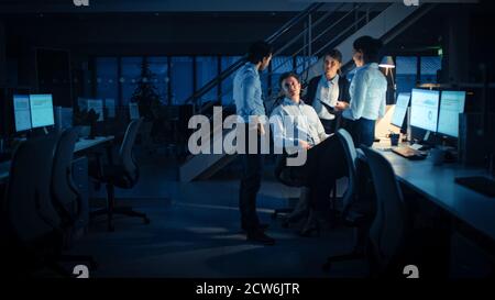 Late at Night In Modern Office: Diverse Team of Successful and Ambitious Businessmen and Businesswomen Work on Computer, Having Discussion, Finding Stock Photo