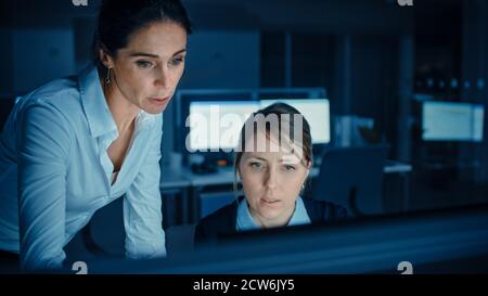 Beautiful Businesswoman Uses Desktop Computer, Consults Her Project Manager about Documents with Graphs and Statistics, Finishing Important Project Stock Photo