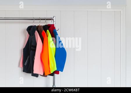 Colorful fleece jackets are hanging on hangers near white wall in a store Stock Photo