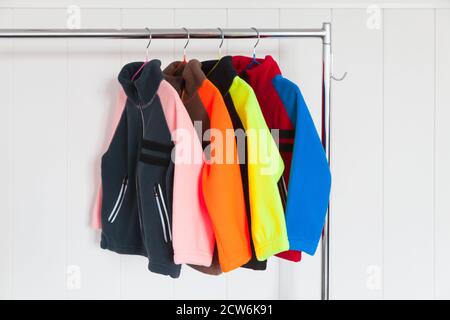 Colorful fleece jackets are hanging on rack near wall Stock Photo