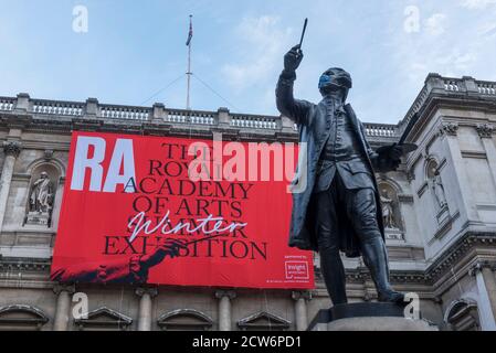 London, UK.  28 September 2020. The masked Joshua Reynolds statue in front of a sign for the Summer Exhibition at the Royal Academy of Arts in Piccadilly which, due to the Covid-19 lockdown, is taking place for the first time in the autumn.  Over 1000 works in a range of media by Royal Academicians, established and emerging artists, feature in the exhibition which runs from 6 October 2020 – 3 January 2021.  Credit: Stephen Chung / Alamy Live News Stock Photo