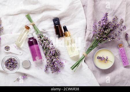Lavender oils, serum liquids butter parfumes, lavender flowers on white fabric. Set skincare spa beauty cosmetic products. Lavender essential oil Stock Photo