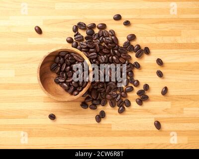 A collection of coffee beans in a wooden bowl and more scattered outside Stock Photo