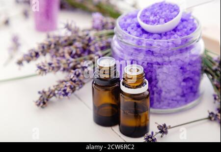 Lavender essential oils and violet sea salt, lavender flowers. Lavender bath products Aromatherapy treatment on white wooden background. Skincare spa Stock Photo