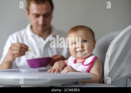 Father feeding baby daughter with spoon in high chair Stock Photo