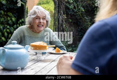 Mature Woman Visiting Lonely Senior Mother In Garden During Lockdown Stock Photo