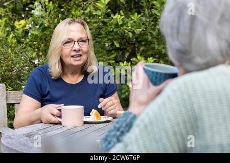 Mature Woman Visiting Lonely Senior Mother In Garden During Lockdown Stock Photo