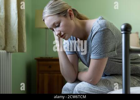Unhappy Woman Suffering With Depression Sitting On Bed Wearing Pyjamas