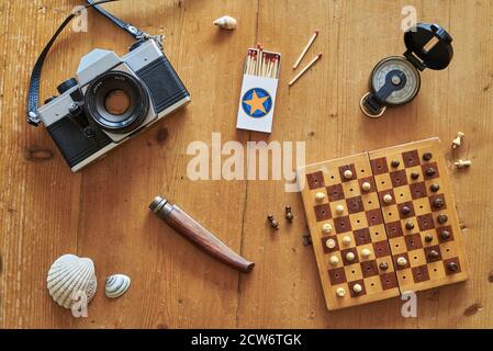 Topview of retro travel equipment on a wooden table. Vintage camera, matches, knife, mussel, chess board and compass on a wooden table. Stock Photo