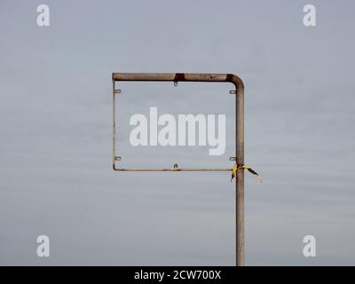 An empty sign frame, possibly a road sign or a traffic sign. The sign itself is missing, and there is a piece of yellow and black plastic tied around Stock Photo