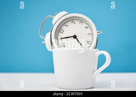 Morning time concept. White retro alarm clock in cup on blue background Stock Photo