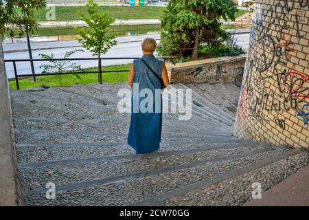 Zrenjanin, Serbia, August 20, 2016. A woman in a long denim dress coming down the stairs. Stock Photo