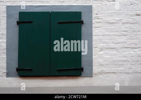 Green wooden window blinds and white stone wall Stock Photo