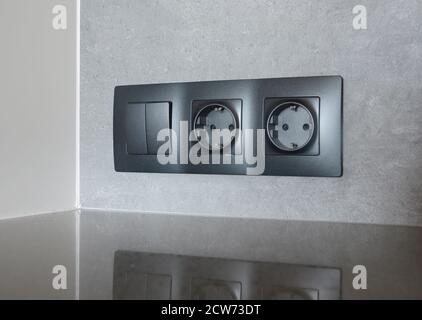 A close-up on black European socket, power outlet plug and light switch on a gray wall in the kitchen. Stock Photo