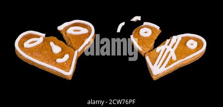 Two broken gingerbreads in heart shape with painted face isolated on black background. Close-up of cracked baked holiday pastries decorated by smiley. Stock Photo