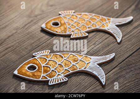 Two golden fish shaped cookies in artistic detail on wood background. Closeup of cute sweet gold fishes for happiness baked from Christmas gingerbread. Stock Photo
