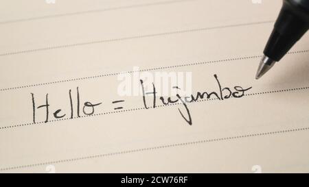 Beginner Swahili language learner writing Hello word Hujambo for homework on a notebook macro shot Stock Photo