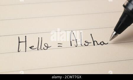 Beginner Hawaiian language learner writing Hello word Aloha for homework on a notebook macro shot Stock Photo