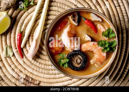 Traditional spicy Thai soup tom yum kung with shiitake mushrooms and prawns, ingredients above on straw wicker napkin as background. Flat lay, space Stock Photo