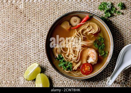 Asian spicy noodles soup with shiitake mushrooms and prawns, ingredients above on straw wicker napkin as background. Flat lay, space. Asian style dinn Stock Photo
