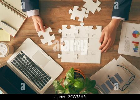 Man sitting at his workplace in the office. Top view close-up. Businessman is trying to connect couple puzzle piece. Symbol of association and connect Stock Photo