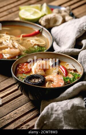 Variety of asian soups. Traditional spicy Thai tom yum kung and noodles soup with shiitake mushrooms, prawns, ingredients above on linen cloth over wo Stock Photo