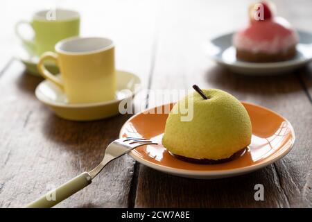 Two Small French ball shaped cakes mousse dome served on a plate with cups of tea Stock Photo