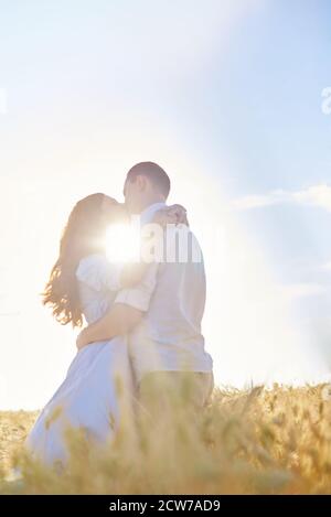 Stylish and modern couple kissing in a wheat field. A young woman hugs her boyfriend and kisses each other. The concept of passion and love. Out of focus. Stock Photo