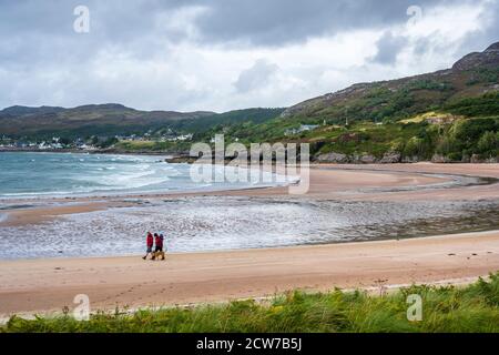Couple walking dog on Gairloch Beach (Gaineamh Mhòr) with coastal town of Gairloch in distance - Gairloch, Wester Ross, Highland Region, Scotland, UK Stock Photo