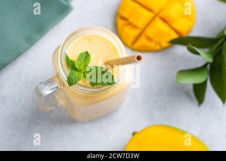 Mango smoothie in glass jar with eco bamboo drinking straw decorated with mint leaf on grey concrete background Stock Photo