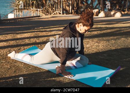 Middle-aged woman doing stretching in the city park on sunset. Female in yoga asana on mat Stock Photo