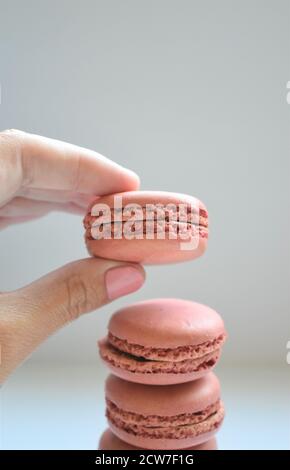 Female caucasian hand with pink nail polish is shown taking a pink french macaron from a stack of three Stock Photo