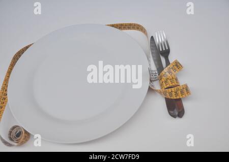 Plate, white plate with yellow measuring tape beside and fork and knife on white background, conceptual photo about weight and diet, Brazil, South Ame Stock Photo