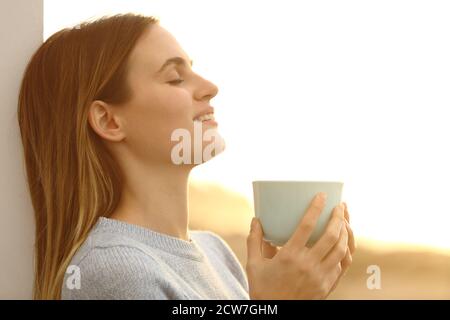 Relaxed woman drinking coffee resting leaing on a wall on the beach at sunset