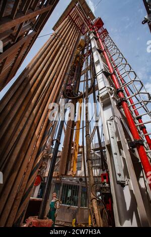 Abstract industrial background of oil deposit. View on oil drilling rig bottom-up. Steel cables, drilling pipes, stair and chain. Oil worker in green. Stock Photo