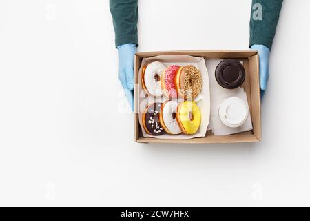 Coffee with sweets for two takeaway during covid outbreak. Waiter in rubber gloves gives box of donuts with glaze and crumb and cups of coffee Stock Photo