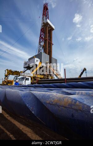 Oil deposit. Works on drilling rig. Blue rusted drilling pipes on front in focus.  Oil worker, truck crane and rig on foreground blurred. Blue sky Stock Photo