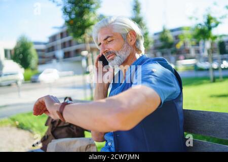 Portrait of mature man sitting outdoors in city, using smartphone. Stock Photo