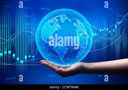 Hand Holding Globe Over Blue Background With Global Economy Graphs Stock Photo